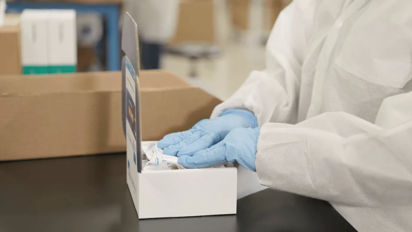 A gowned DS2 team member assembling a specimen collection kit
