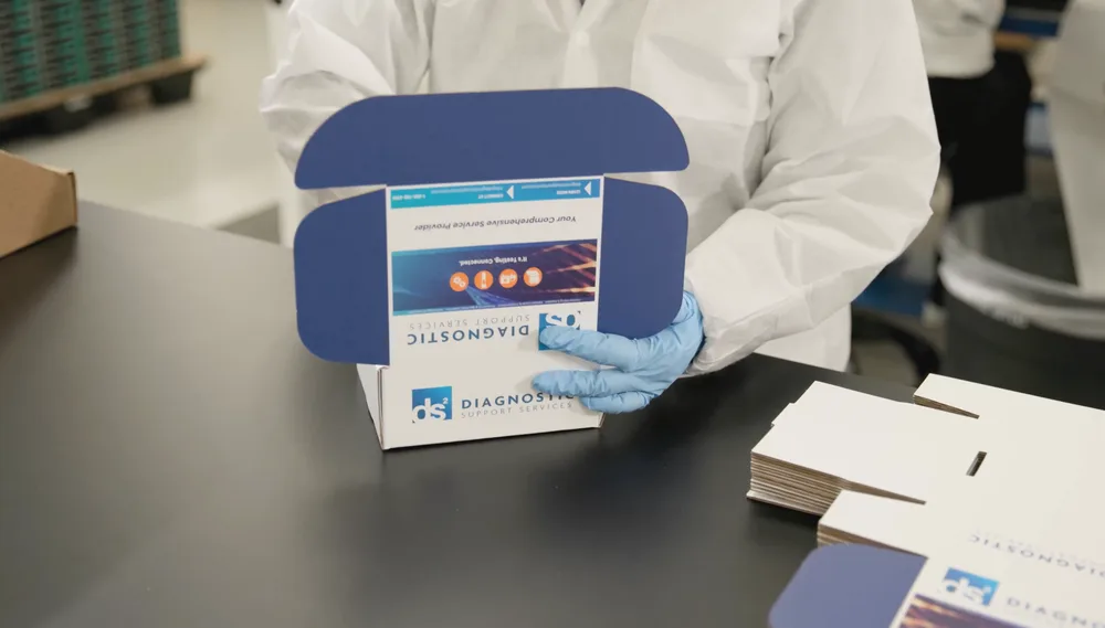 A gowned DS2 team member assembling a branded specimen collection kit